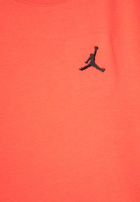 Korálově zbarvené bavlněné tričko s černě vyšitým logem Jumpman na levé části hrudi. Hladká textura, design s kulatým výstřihem.