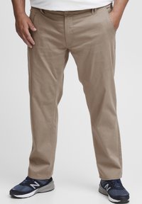 Khaki cotton trousers with a straight fit, featuring belt loops and side pockets. Worn with navy athletic shoes. Smooth texture.