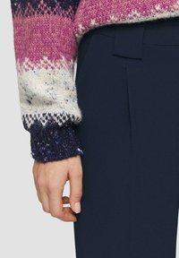 Gebreide trui met een verloop van roze, blauw en crème, afgewerkt met een gestructureerde marineblauwe manchet. Gecombineerd met donker marineblauwe pantalon.