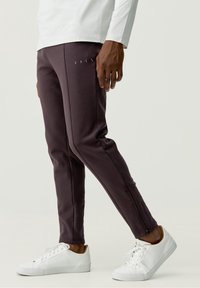 Mörklila träningsbyxor med sidoglatta, tillsammans med vita sneakers. Tyget ser mjukt ut med en slät textur och en figurnära design.