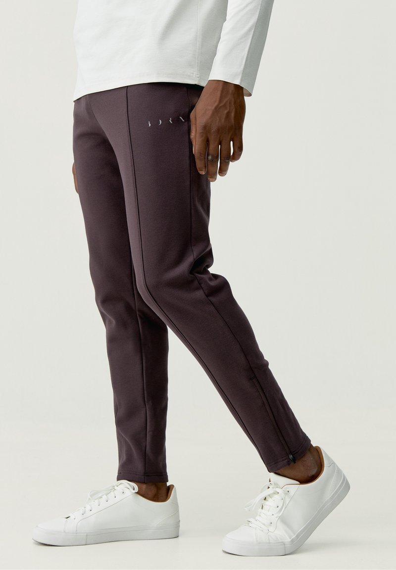 Mörklila träningsbyxor med sidoglatta, tillsammans med vita sneakers. Tyget ser mjukt ut med en slät textur och en figurnära design.