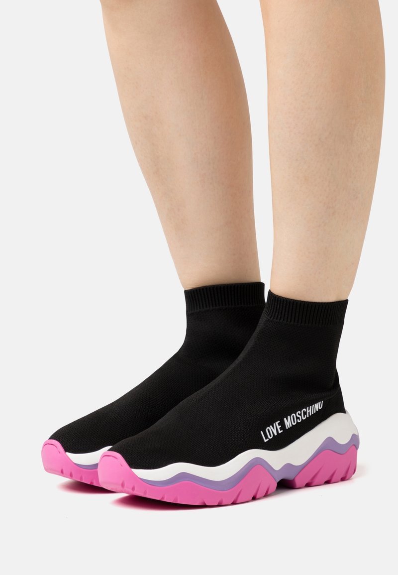 Black knitted sock sneakers with a white, pink, and purple wave-patterned sole. Features "LOVE MOSCHINO" text on the side.