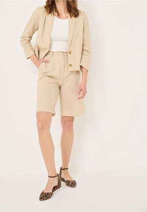 Beżowa lniana marynarka z dwoma złotymi guzikami, w połączeniu z beżowymi dopasowanymi szortami i balerinami w zwierzęcy wzór. Gładka faktura i strukturalny design.