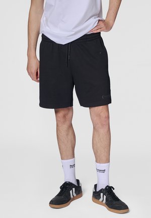 Svarta bomullsshorts med elastisk midja och dragsko. Kombinerade med svarta sneakers och vita strumpor med en varumärkeslogotyp.
