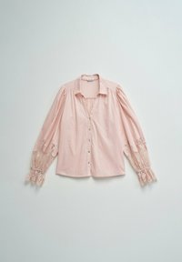 Blusa rosa claro abotonada con mangas abullonadas que presentan detalles de encaje y puños con volantes, extendida sobre una superficie pálida.