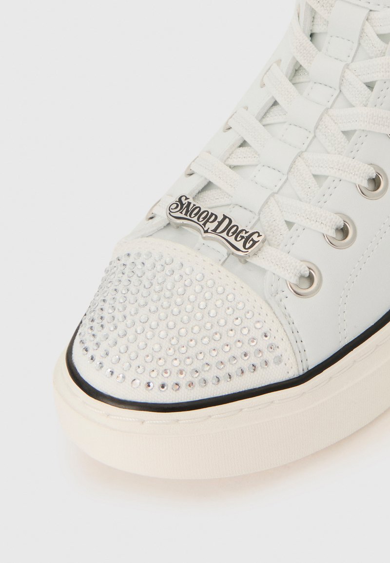 Sneaker bianco con accenti di strass sulla punta, caratterizzato da una forma arrotondata, lacci in tessuto e un'etichetta del logo "SnoopDog" in argento.