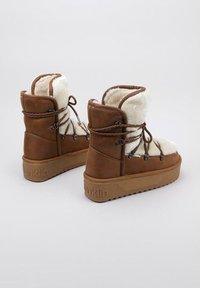 Botas de cuero sintético marrón con un forro blanco esponjoso, puntera redonda y suelas de goma gruesa. Presentan ganchos metálicos para los cordones y detalles de costura.
