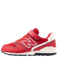 Baskets New Balance rouges et blanches avec lacets et une sangle Velcro, semelle noire et détails cousus, présentées de côté sur un fond blanc.
