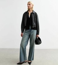 Giacca cropped in pelle sintetica nera, top nero, jeans larghi azzurri chiari e scarpe con tacco nere appuntite con una borsa nera texture.