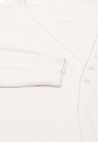 Lichtbeige cardigan van zachte stof. Beschikt over een V-hals, zes knopen, geribde manchetten en een lichte textuur met voorzakken.