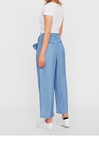 Ljusblå, vida byxor i denim. Har en mjuk textur, en knytbelten, fickor och en avslappnad passform. Matchas med vita sneakers.