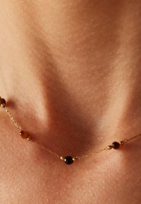 Gouden ketting met ronde amber kralen en gouden accenten, rustend op de huid met zichtbare textuur en contouren.