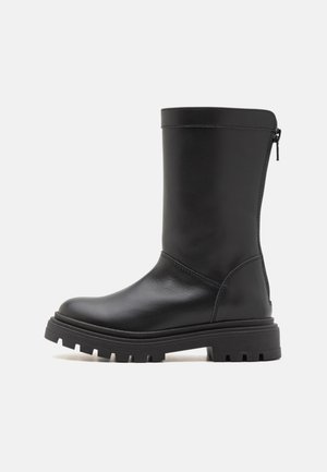 Black leather knee-high boots with a smooth surface, chunky rubber sole, and side zipper. Features a rounded toe and minimal stitching.