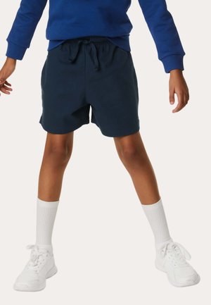 Shorts di cotone blu navy con cintura elasticizzata e coulisse. Indossati con calzini bianchi al ginocchio e scarpe da ginnastica bianche.
