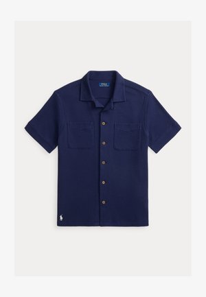 Tummansininen lyhythihainen nappikauluspaita, jossa kaksi rintataskua, teksturoiduilla kankailla ja pieni valkoinen kirjailtu Polo-logo helmassa.