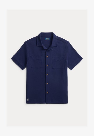 Πουκάμισο στενό, κοντομάνικο σε ναυτικό μπλε χρώμα με δύο τσέπες στο στήθος, υφή υφάσματος και μικρό λευκό κεντητό λογότυπο Polo στο τελείωμα.