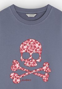 Camiseta de algodón gris con un gráfico de calavera y tibias cruzadas florales en rosa. Corte holgado con cuello acanalado, nombre de la marca "Scalpers" impreso debajo.