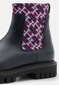 Černá kožená bota s tlustou podrážkou a červenou, bílou a modrou vzorovanou tkaninovou panelem v oblasti horní části kotníku.