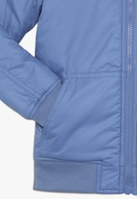 Jasnoniebieska puchowa kurtka z zamkiem błyskawicznym, ściągaczami przy mankietach i bocznymi kieszeniami. Gładka faktura i pikowany design zapewniają izolację.