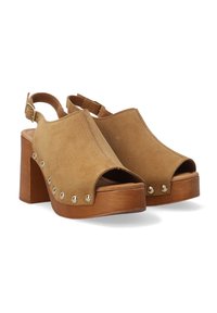 Open-toe platform sandalen in beige suède met een gebogen ontwerp, voorzien van gouden studs aan de zijkant en een stevige houten hak.