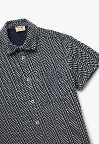 Camicia a maniche corte, botton down, in pattern a quadri houndstooth blu navy e bianco, con colletto e taschino sul petto, dotata di bottoni bianchi.