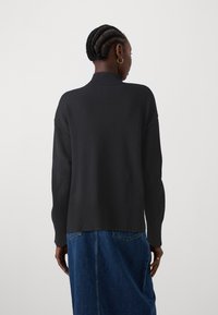 Pull en tricot noir avec un col montant, détails côtelés à l'ourlet et aux poignets, associé à une jupe en denim. Texture lisse et coupe décontractée.