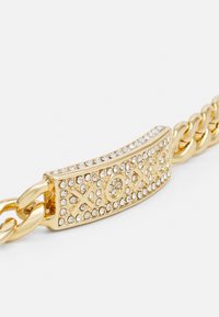 Zlati zapestnica z velikim, strukturiranim povezovalnim delom, okrašena s prozornimi rhinestones in graviranim vzorcem "XOXO".