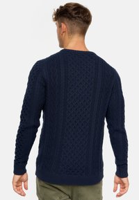 Navy knitted sweater with a textured cable pattern, ribbed cuffs, and hem. Fit is standard with a round neckline.