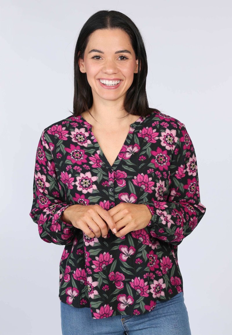 Schwarze Bluse mit pinkem und weißem Blumenmuster, V-Ausschnitt, Knopfdetails und langen Ärmeln. Kombiniert mit blauen Jeans.