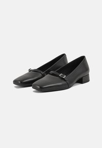 Chaussures à talons blocs en cuir noir avec bout carré et une fine bride ornée d'une petite boucle métallique.