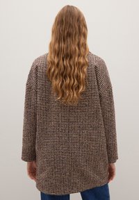 Abrigo a cuadros marrón y púrpura con mangas largas, ajuste holgado, tela texturizada y dobladillo recto, mostrado desde atrás.