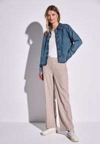 Chaqueta de mezclilla, azul claro, diseño de botones. Camiseta blanca debajo, pantalones de pierna ancha beige. Zapatillas blancas. Texturas suaves, aspecto casual.