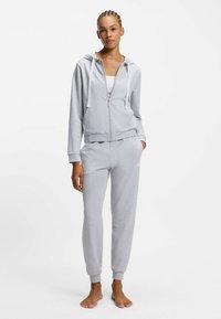 Harmaa vetoketjullinen huppari, jossa on kiristysnyörit ja etutasku, yhdistettynä vastaaviin kapealahkeisiin collegehousuihin. Molemmat valmistettu pehmeästä, kevyestä kankaasta.