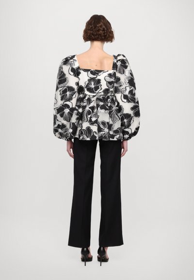 Blusa de flores en blanco y negro con mangas abullonadas, cintura ceñida, combinada con pantalones anchos negros y zapatos de tacón.