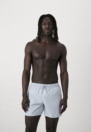 Light blue swim shorts with an elastic waist and drawstring, made of smooth fabric, worn by a person with a shirtless, athletic build.
