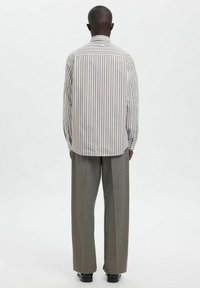 Stripete skjorte med knapper i lys krem og brun. Lange ermer, avslappet passform og en bakre ryggskjøt. Kombinert med grå plissert bukse.