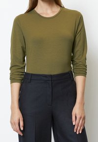 Långärmad, olivgrön topp i ett mjukt tyg med rund halsringning. Kombinerad med mörkblå skräddarsydda byxor som har en avslappnad passform.