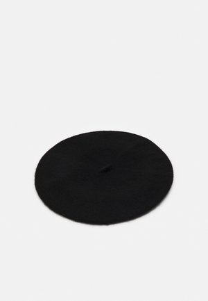 Schwarzes Wollbaret mit kleinem Stiel in der Mitte, flach auf einer weißen Oberfläche liegend.