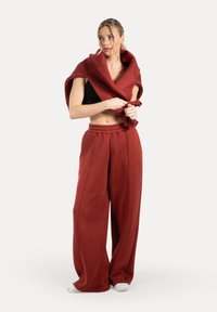 Červené, široké tepláky z měkkého materiálu s elastickým pasem. Spárované s odpovídajícím oversize svetrem přehozeným přes ramena.