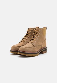 Botas de tobillo de ante en tono marrón con diseño de cordones, puntera redonda y suela de goma en contraste con agarre texturizado. Asa en el talón.