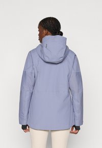 Vaalean lilac vedenpitävä takki hupulla, jossa on teksturoitu pinta ja pitkät hihat. Takana on selkeälinjainen muotoilu ilman näkyviä koristeita.