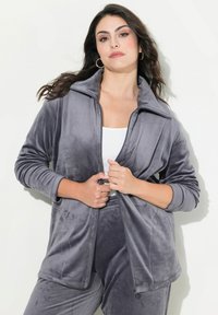 Giacca in pile grigia con zip, colletto alto, maniche lunghe e vestibilità comoda. La trama appare morbida e liscia, ideale per un look informale.