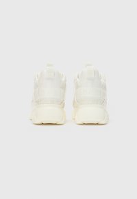 Baskets de sport blanches avec une tige texturée et des accents lisses. Le design comprend un collier rembourré et un branding contrasté sur le talon.