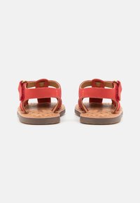Røde sandaler med åpen design, justerbar stropp og tan fotseng med stjerne mønster. Gummisåle for grep og komfort.