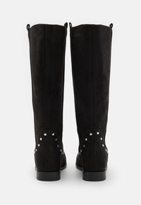 Botas de ante negras hasta la rodilla con una textura suave, con tachuelas plateadas a lo largo del área del tobillo y pequeñas asas en la parte superior.