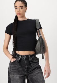 Černé zkrácené tričko s krátkými rukávy v kombinaci s šedými džíny s vysokým pasem. Modelka nese strukturovanou šedou kabelku na rameno.