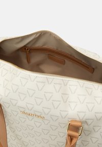 Valentino rokassoma ar teksturētu krēmkrāsas virsmu, zelta logotipu un brūniem ādas akcentiem. Satur kabatu ar rāvējslēdzēju un gludu oderi.