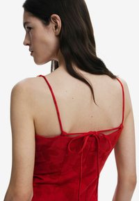 Punane kleit õhukeste rihmadega, tekstuuriga kangas, millel on lillemuster, reguleeritav side seljaosas ja struktureeritud bodice disain.
