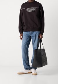 Sudadera negra con el logo "HUGO", jeans azules, zapatillas blancas y un gran bolso tote negro con el lettering en relieve "HUGO". Atuendo casual.