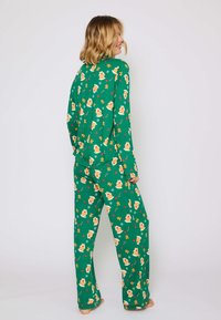 Groene pyjama set met een patroon van een peperkoekhuisje en sneeuwvlokken, lange mouwen en losse broekspijpen. Zachte stof met een gladde textuur.